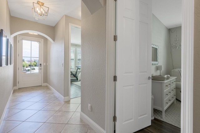 entryway featuring a notable chandelier, light tile patterned flooring, arched walkways, and baseboards