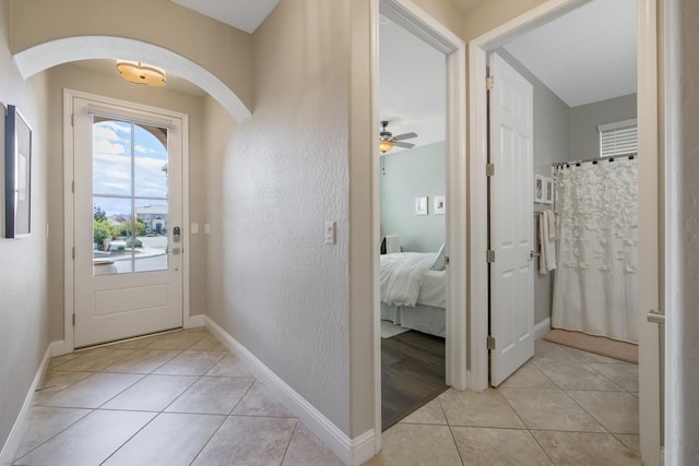 doorway featuring light tile patterned floors, arched walkways, a ceiling fan, and baseboards