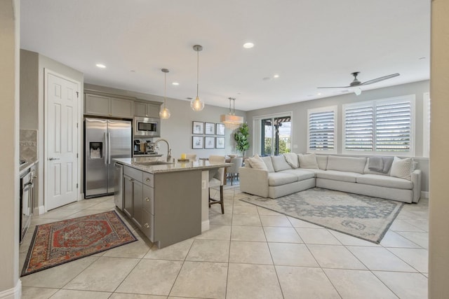 kitchen featuring a breakfast bar area, light tile patterned floors, gray cabinets, appliances with stainless steel finishes, and a sink