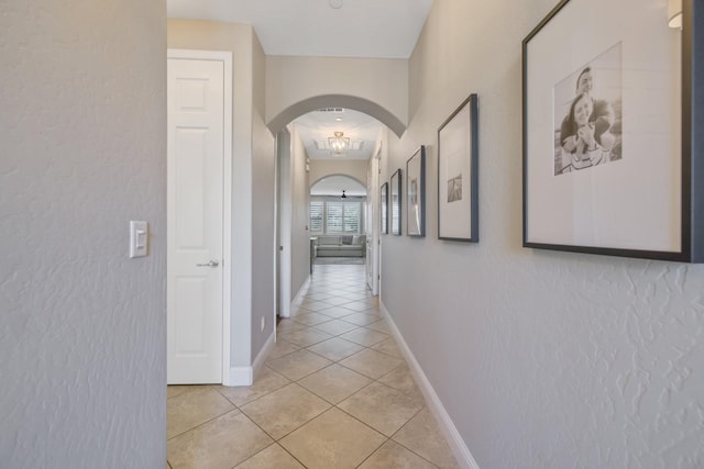 hallway with light tile patterned floors, baseboards, and arched walkways