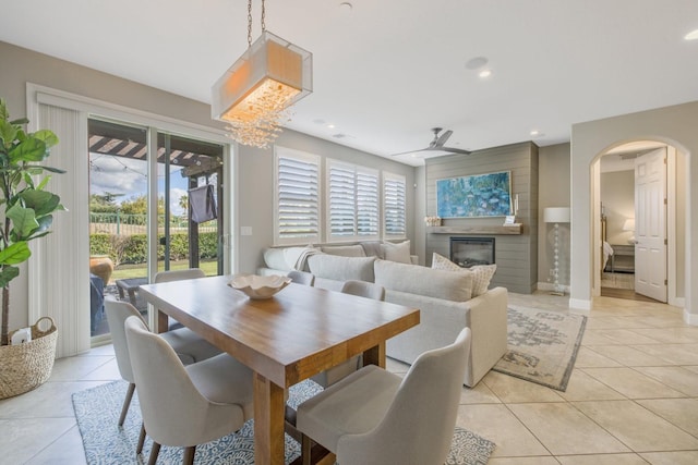 dining room featuring light tile patterned floors, arched walkways, a glass covered fireplace, and ceiling fan