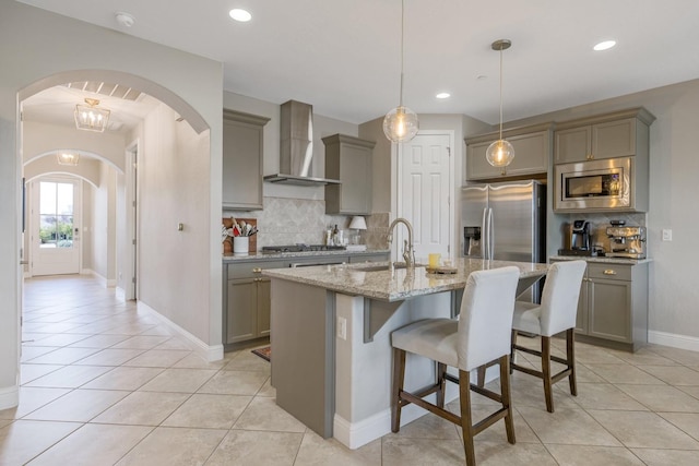 kitchen featuring gray cabinetry, a kitchen breakfast bar, appliances with stainless steel finishes, wall chimney exhaust hood, and light stone countertops