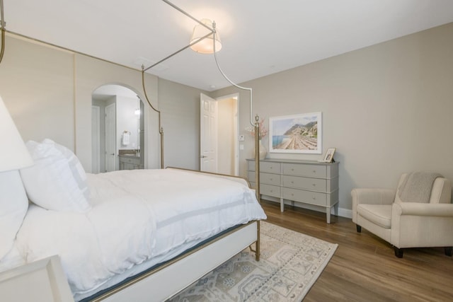 bedroom with arched walkways, ensuite bathroom, baseboards, and wood finished floors