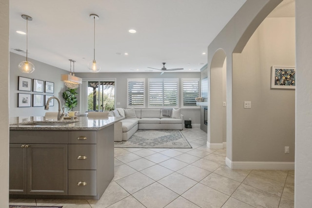 kitchen with light stone countertops, light tile patterned floors, recessed lighting, arched walkways, and a sink