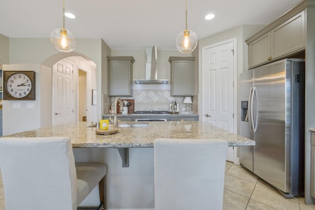 kitchen with arched walkways, gray cabinets, a sink, stainless steel appliances, and wall chimney range hood