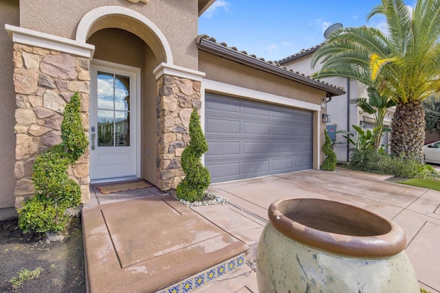 doorway to property with a garage, stone siding, driveway, and stucco siding