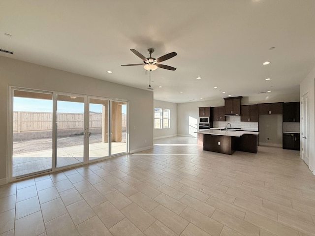 kitchen with a center island with sink, a sink, open floor plan, dark brown cabinetry, and decorative backsplash