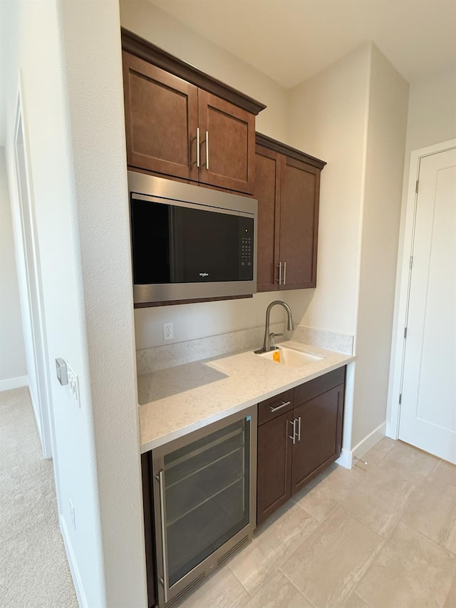 kitchen with beverage cooler, a sink, stainless steel microwave, baseboards, and dark brown cabinets