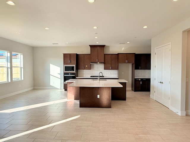 kitchen featuring a sink, built in microwave, backsplash, and an island with sink