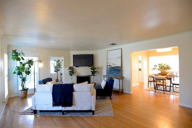 living room with a brick fireplace, light wood-style flooring, baseboards, and visible vents