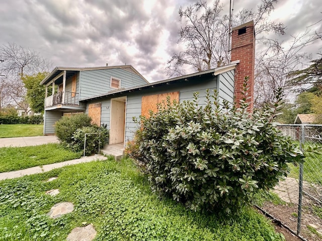 view of front of house featuring a chimney, a balcony, and fence