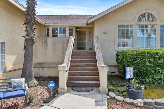 property entrance with stucco siding and a shingled roof