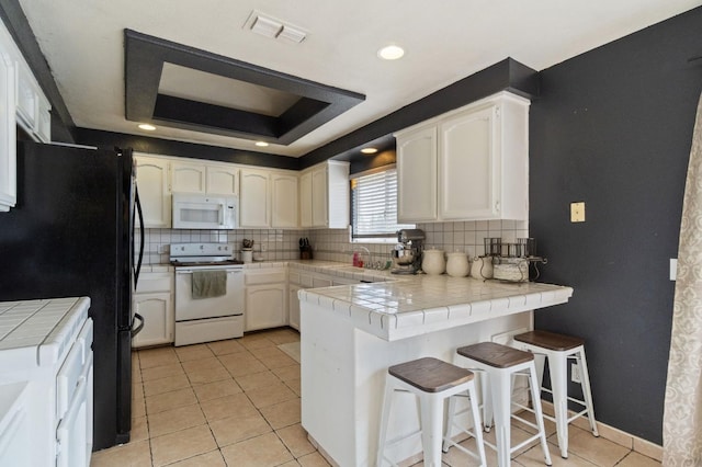 kitchen with visible vents, tile countertops, white appliances, a peninsula, and a raised ceiling