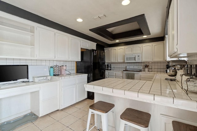 kitchen with white appliances, tile countertops, light tile patterned floors, a peninsula, and a raised ceiling