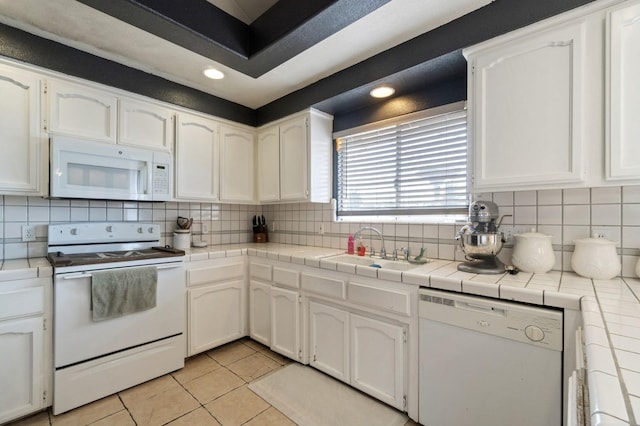 kitchen featuring backsplash, white appliances, white cabinetry, and a sink