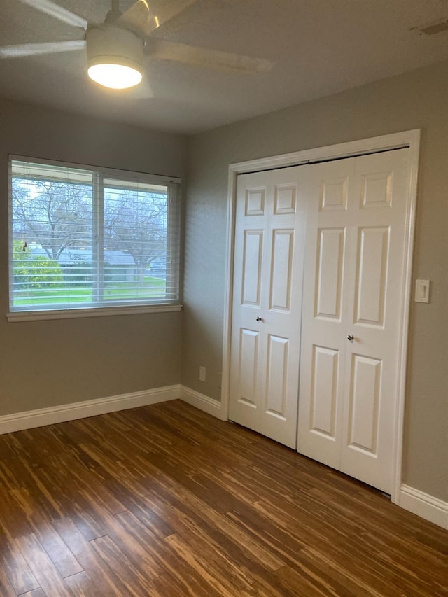 unfurnished bedroom with a closet, baseboards, dark wood-type flooring, and ceiling fan