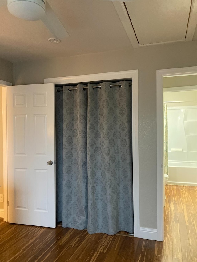 unfurnished bedroom featuring a closet, attic access, baseboards, and wood finished floors