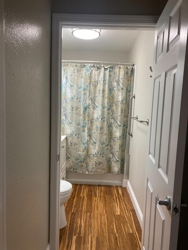 full bathroom with baseboards, toilet, wood finished floors, vanity, and shower / bathtub combination with curtain