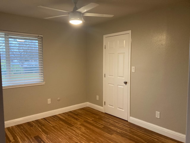 spare room with baseboards, dark wood-style floors, and a ceiling fan