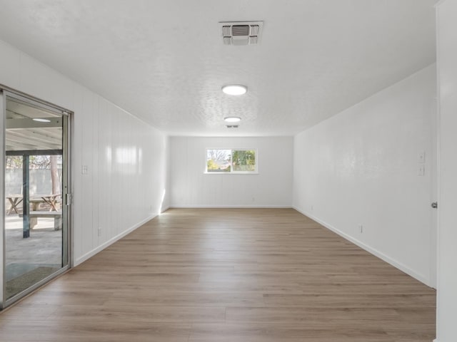 empty room featuring light wood finished floors, visible vents, a textured ceiling, and baseboards