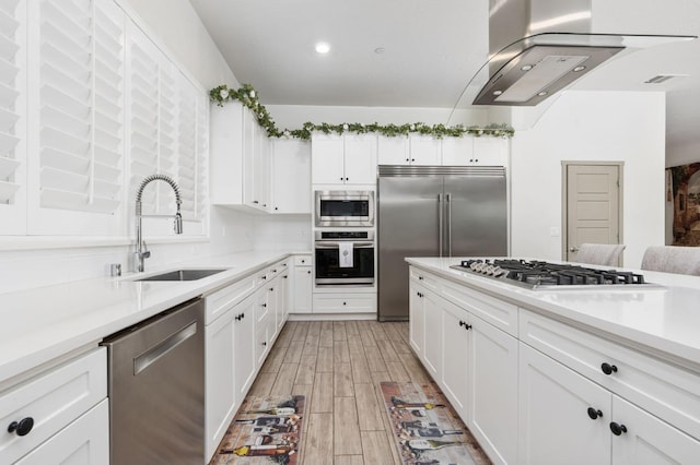 kitchen with a sink, light wood-style floors, white cabinets, light countertops, and built in appliances