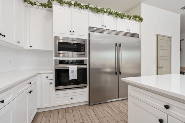 kitchen with built in appliances, white cabinetry, and light countertops