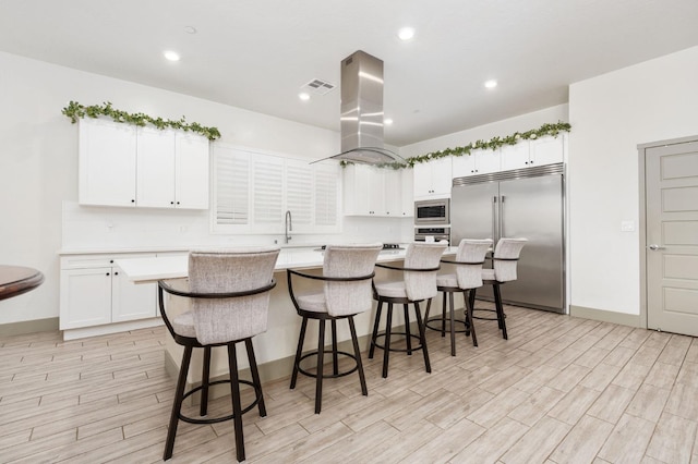 kitchen featuring island exhaust hood, built in appliances, a kitchen island, and light countertops