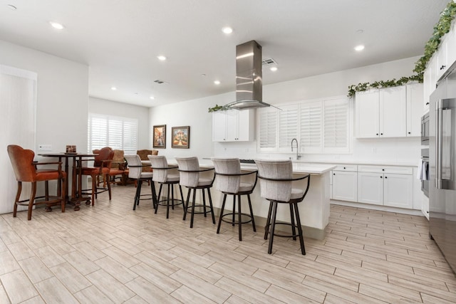 kitchen with a kitchen bar, island range hood, and white cabinetry