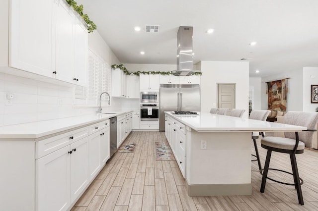 kitchen featuring visible vents, a center island, built in appliances, island range hood, and a sink