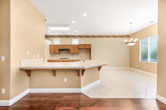 2565 Powers Ave, Clovis, CA 93619 - kitchen with range hood, an inviting chandelier, a breakfast bar, brown cabinets, and tile countertops