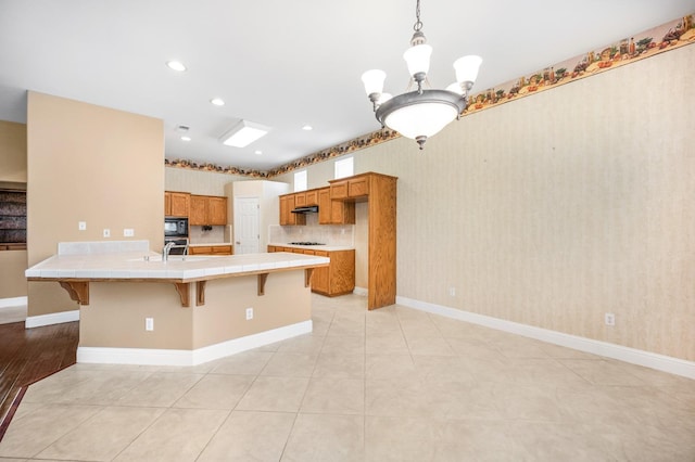 2565 Powers Ave, Clovis, CA 93619 - kitchen featuring a kitchen breakfast bar, tile counters, brown cabinetry, black microwave, and stainless steel oven