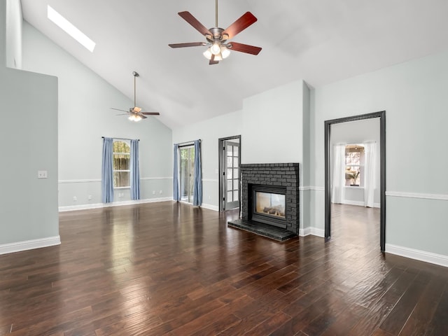 unfurnished living room featuring wood finished floors, high vaulted ceiling, a skylight, ceiling fan, and a brick fireplace