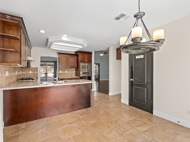 kitchen featuring visible vents, a peninsula, a sink, decorative backsplash, and appliances with stainless steel finishes