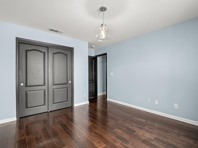 unfurnished bedroom featuring a closet, visible vents, baseboards, and dark wood-style flooring