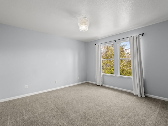 carpeted spare room featuring baseboards, a textured ceiling, and an inviting chandelier