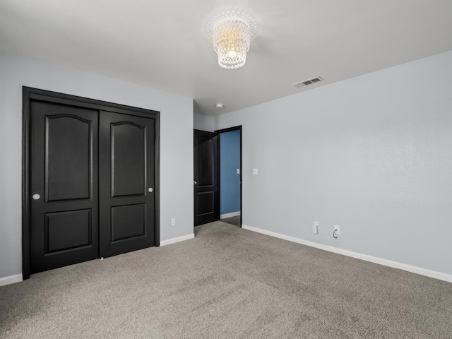 unfurnished bedroom featuring carpet, visible vents, baseboards, a closet, and a notable chandelier