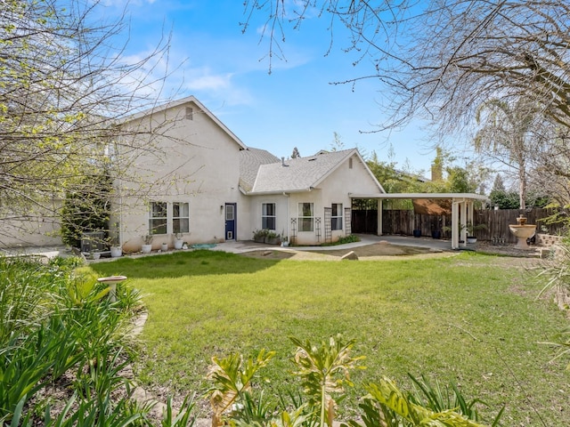 rear view of property with an attached carport, a shingled roof, fence, stucco siding, and a yard