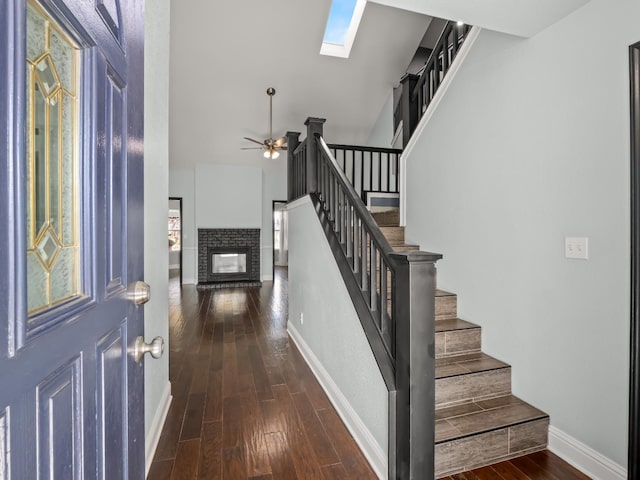 entryway featuring stairway, wood finished floors, baseboards, a skylight, and a fireplace