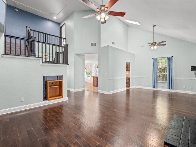 unfurnished living room with a wealth of natural light, visible vents, a ceiling fan, wood finished floors, and stairs