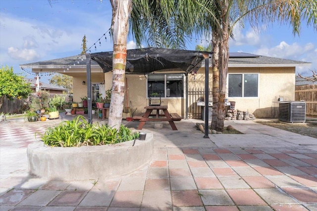 rear view of property featuring stucco siding, central AC, fence, solar panels, and a patio area