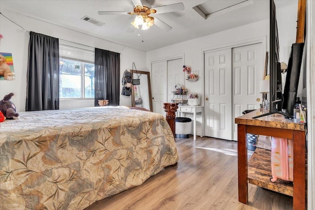 bedroom featuring visible vents, multiple closets, light wood finished floors, attic access, and ceiling fan