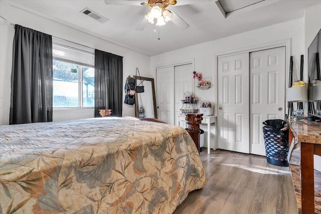 bedroom with visible vents, multiple closets, wood finished floors, and a ceiling fan