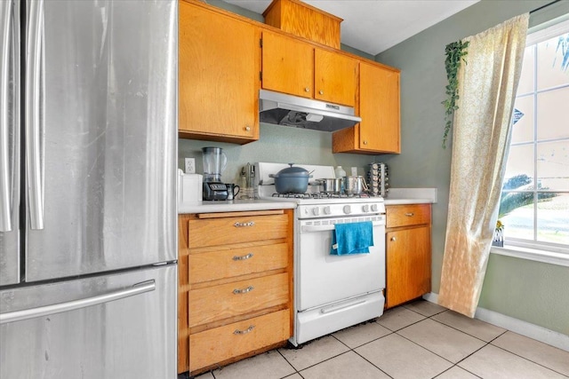 kitchen with under cabinet range hood, white gas range oven, freestanding refrigerator, light tile patterned flooring, and light countertops