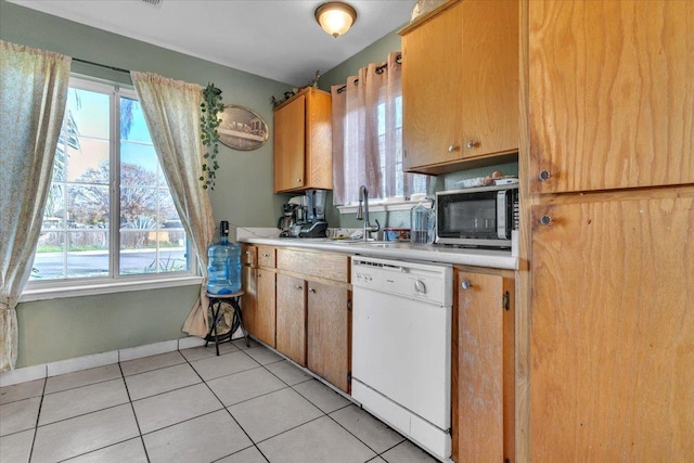 kitchen featuring a sink, stainless steel microwave, white dishwasher, light countertops, and a healthy amount of sunlight