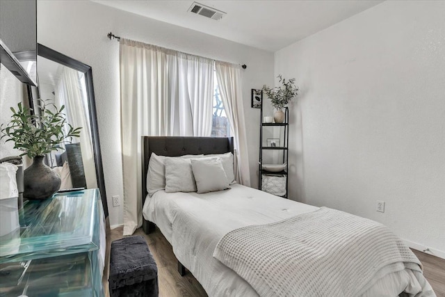 bedroom featuring wood finished floors, visible vents, and a textured wall