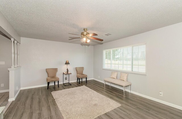 sitting room featuring wood finished floors, visible vents, ornate columns, and baseboards