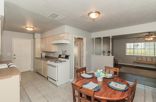 kitchen with light tile patterned floors, visible vents, gas range gas stove, under cabinet range hood, and a textured ceiling