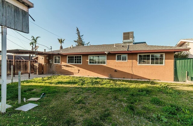 rear view of house with fence, stucco siding, cooling unit, a lawn, and a patio area