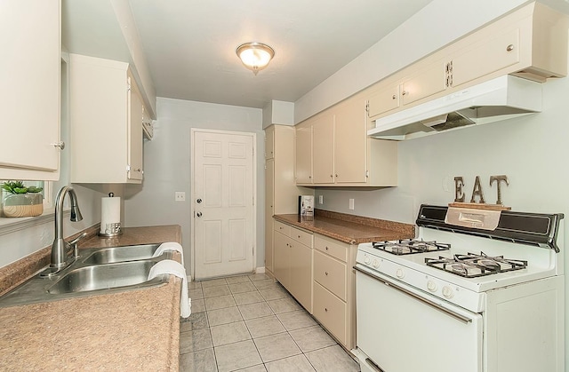 kitchen featuring under cabinet range hood, light tile patterned flooring, gas range gas stove, and a sink