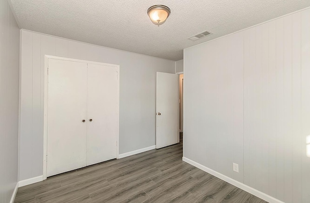 unfurnished bedroom featuring wood finished floors, visible vents, a closet, and a textured ceiling